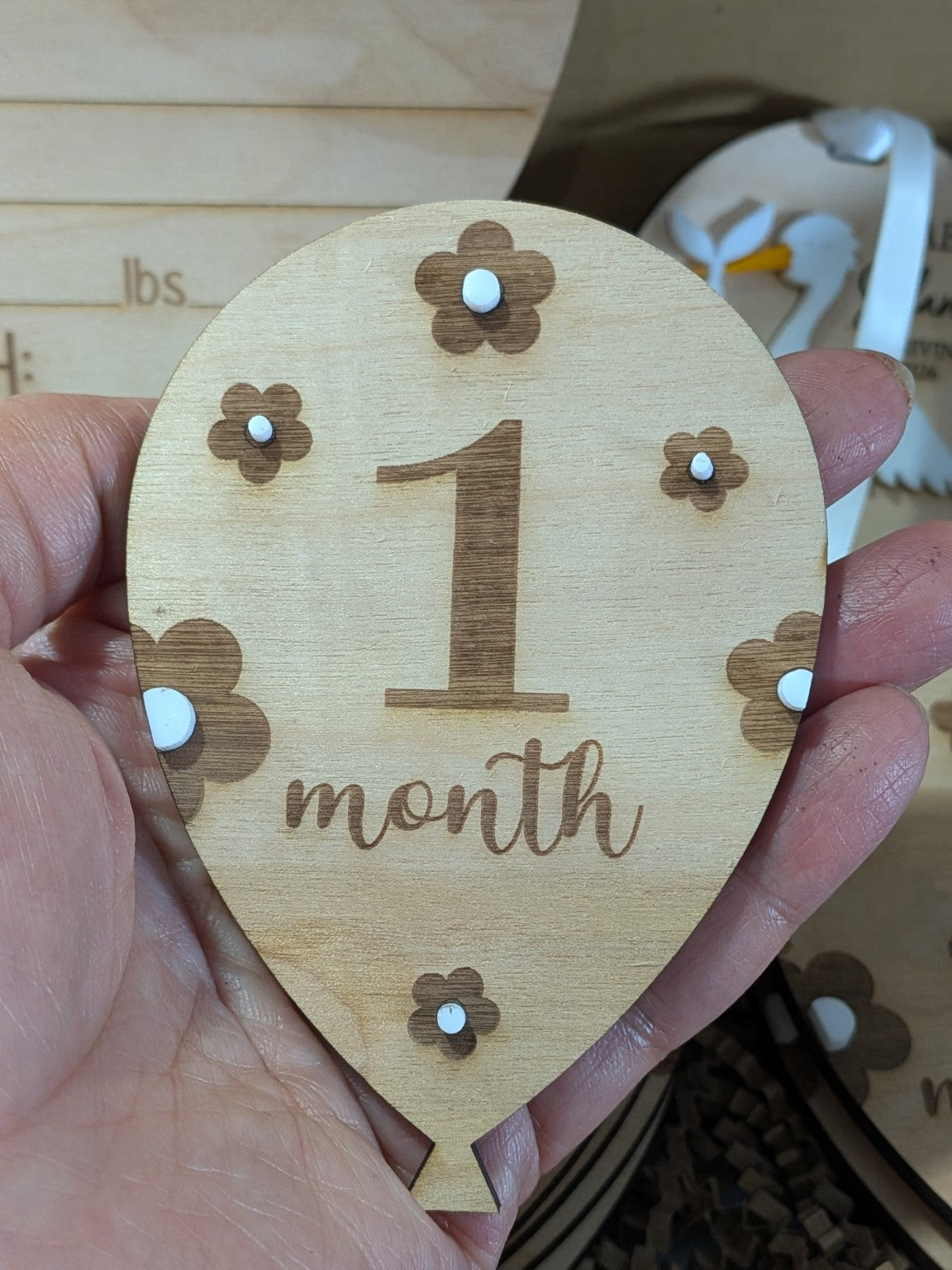 Balloon-shaped wooden monthly milestone marker with floral engraving and raised white flower centres