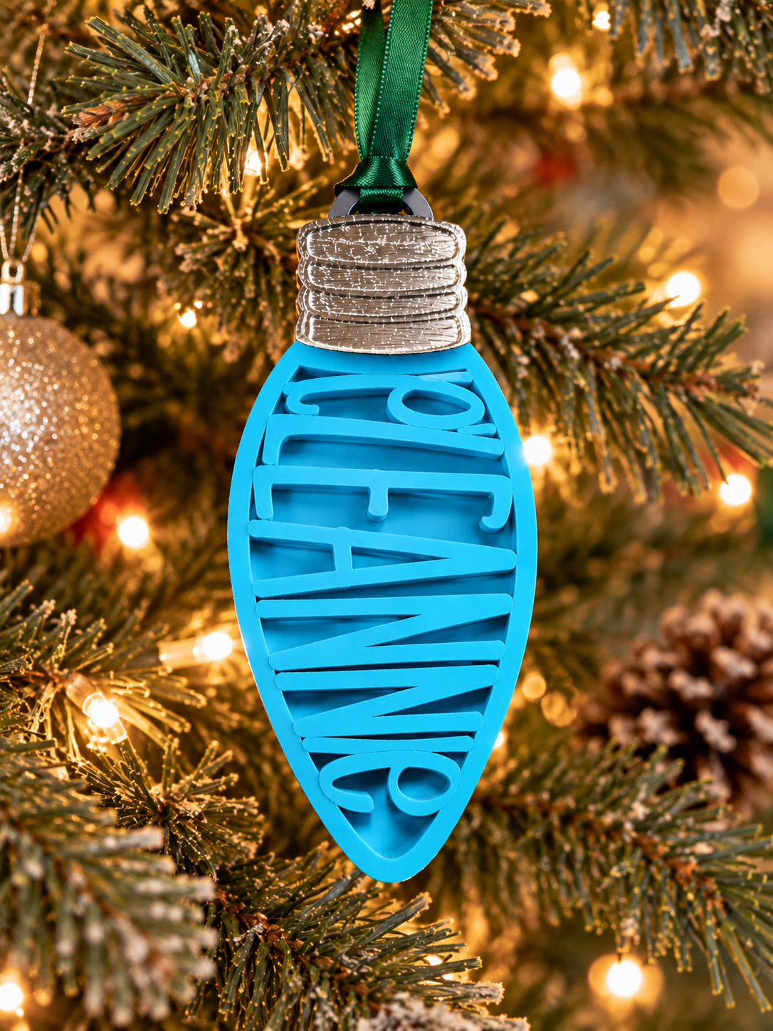 Personalized cerulean blue Christmas light bulb name ornament hanging on a Christmas tree